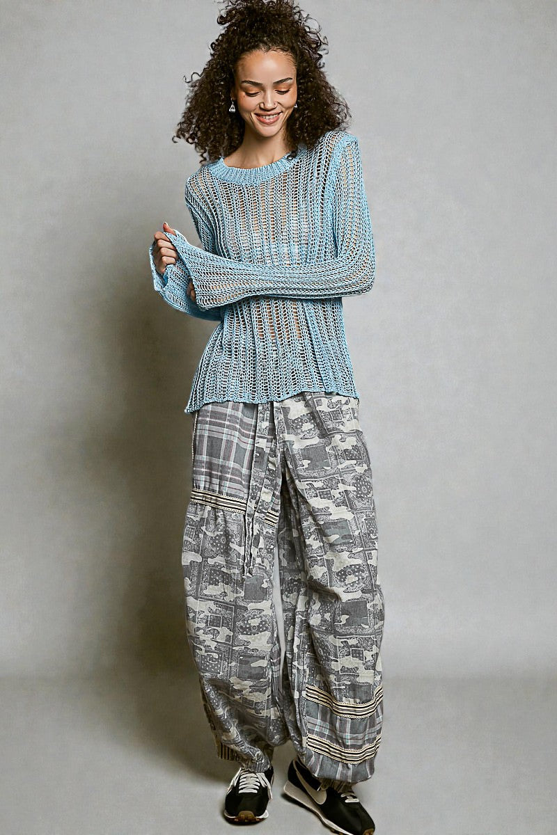 Woman wearing a textured blue sweater and patterned gray pants against a plain background