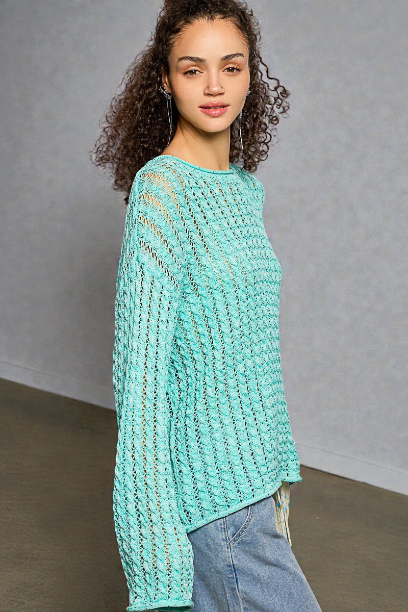 Woman wearing a teal crochet sweater against a plain background