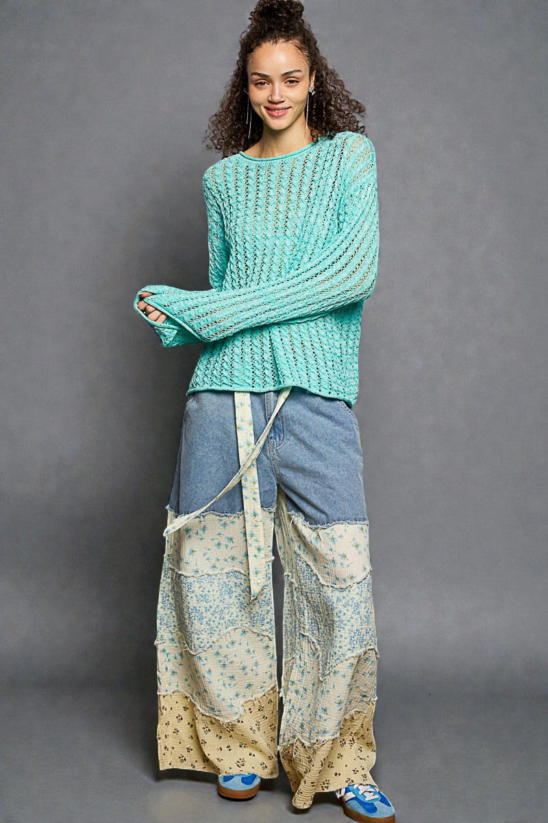 Woman wearing a teal sweater and patchwork pants against a gray background
