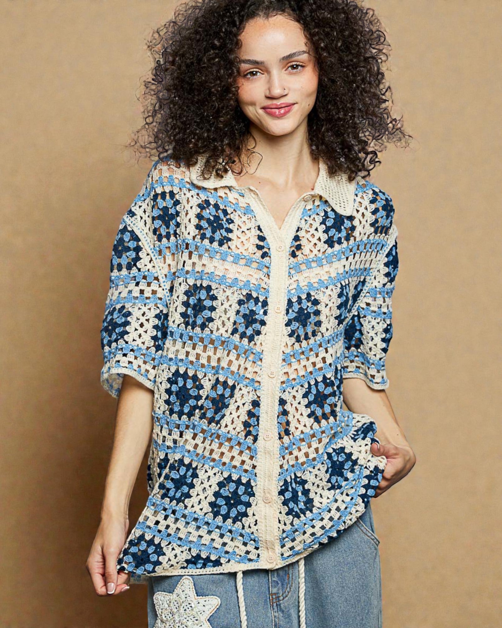 Woman wearing a blue and white patterned crochet shirt against a beige background