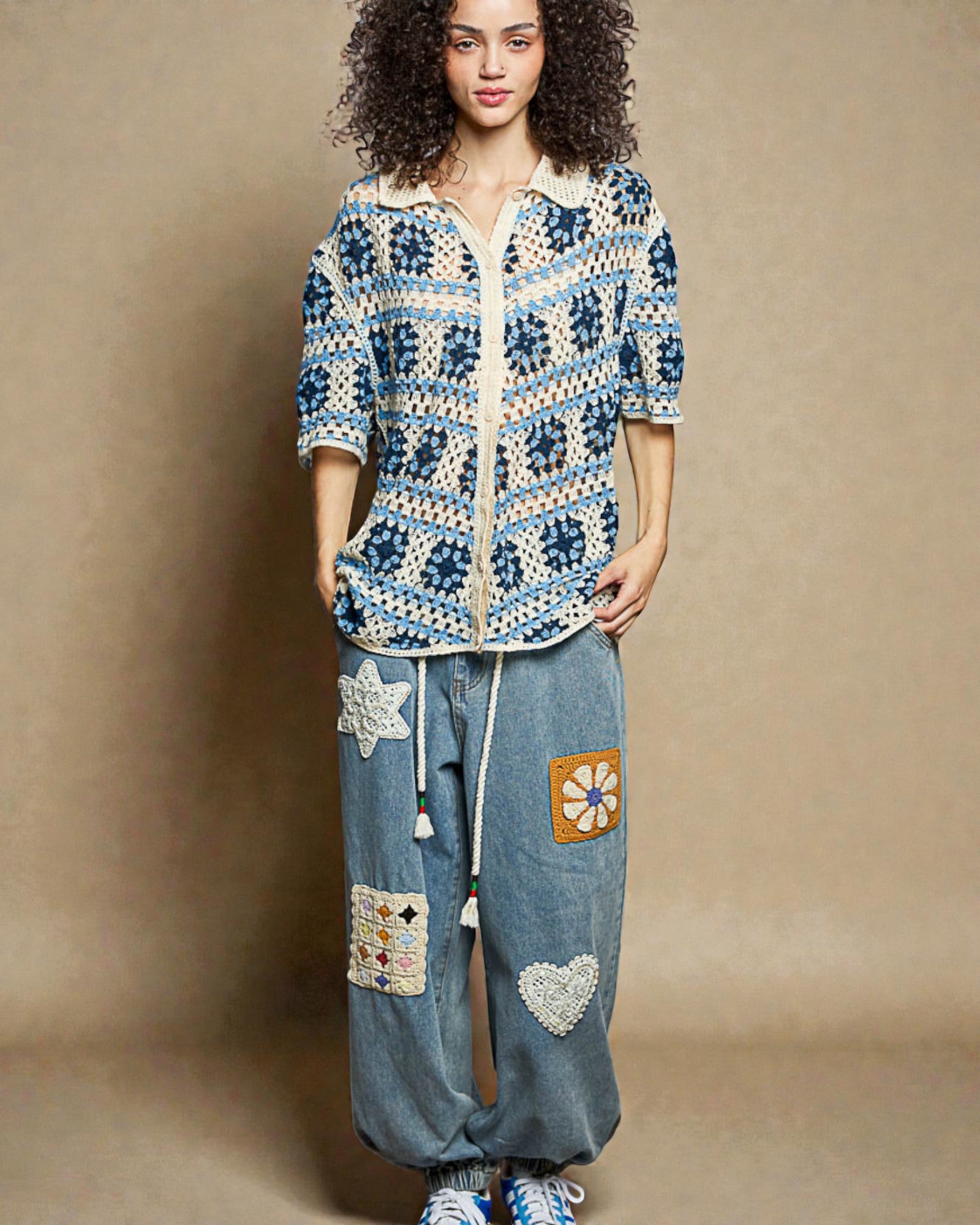 Woman wearing a colorful crochet jacket and denim pants with patches on a beige background