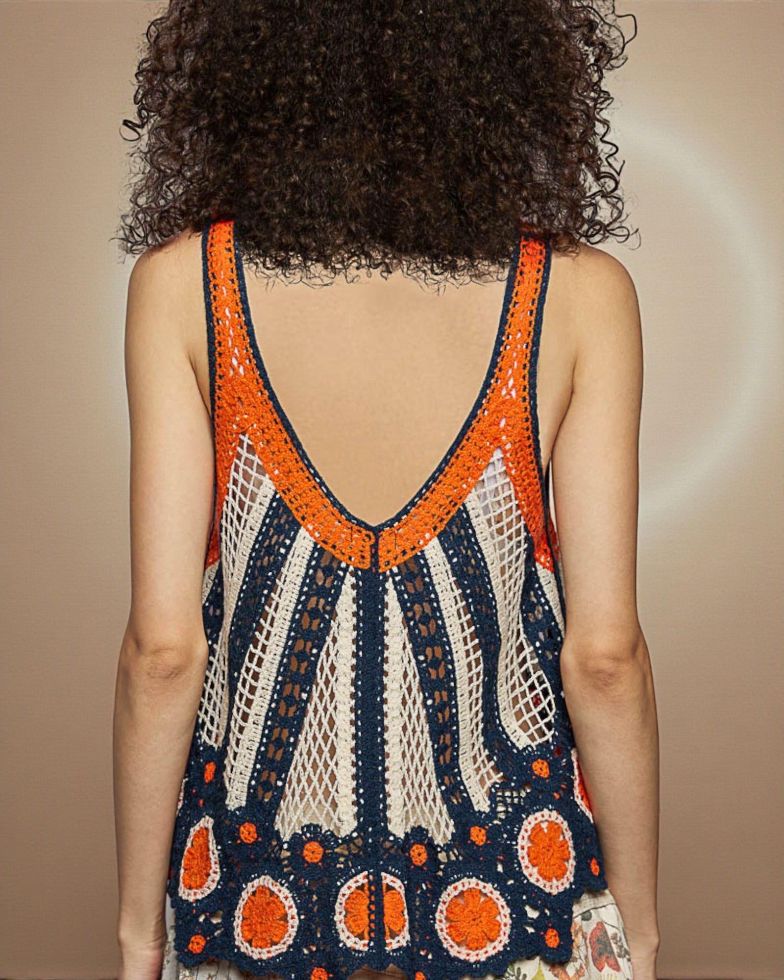 Person wearing a colorful crochet dress with an open back on a beige background