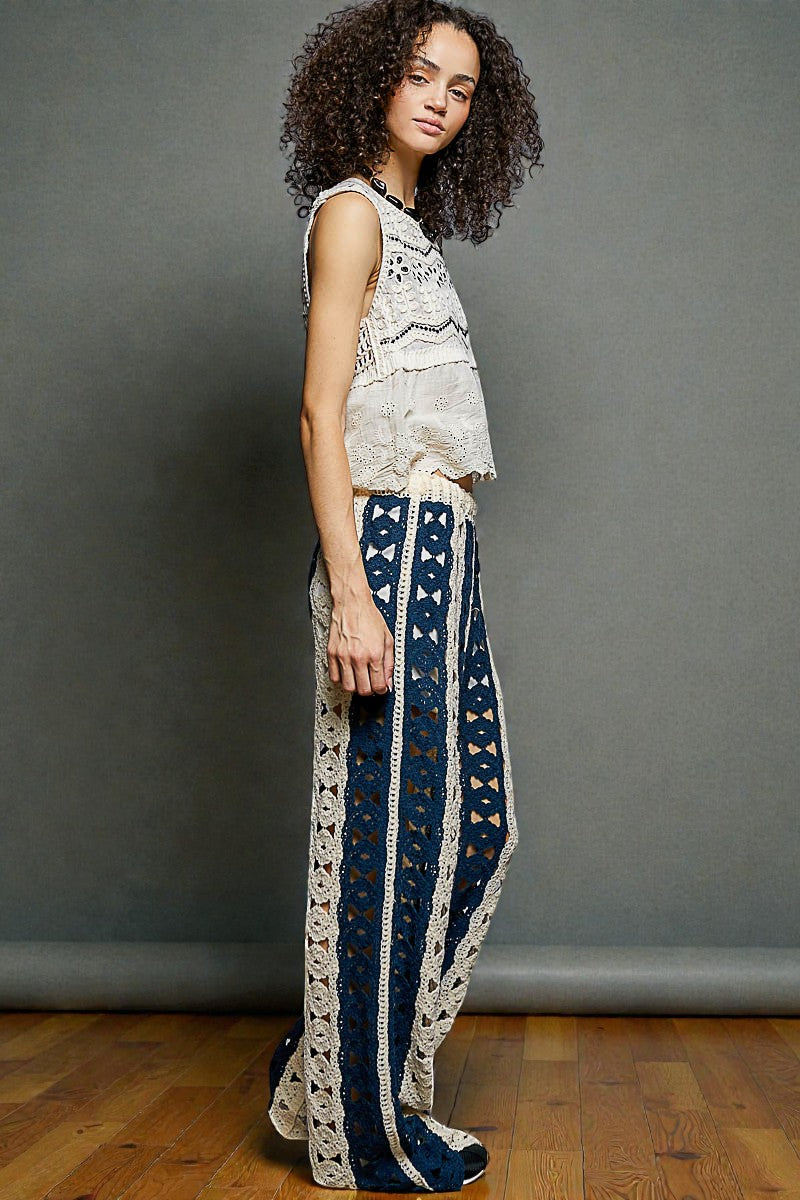 Woman wearing a sleeveless top and patterned pants against a gray wall.