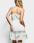 Woman wearing a white dress with green embroidery on a plain background