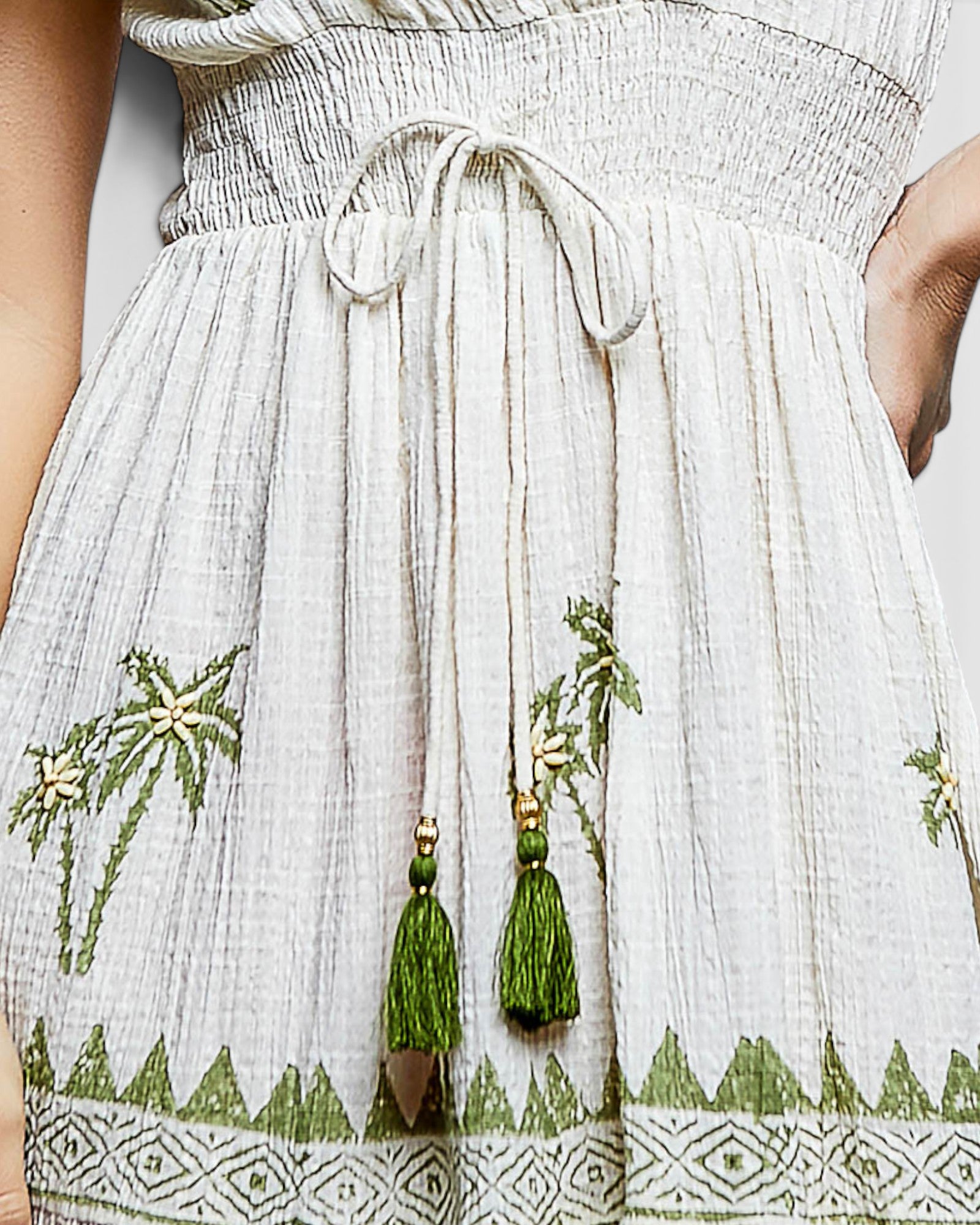 White dress with green embroidery and tassels on a plain background