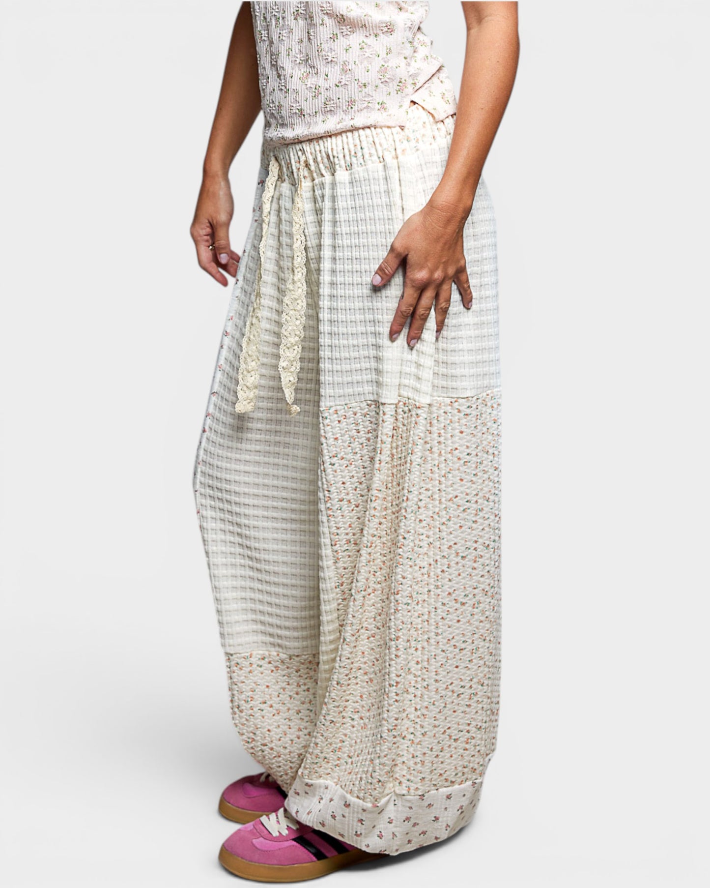 Person wearing a patterned top and light-colored wide-leg pants on a white background
