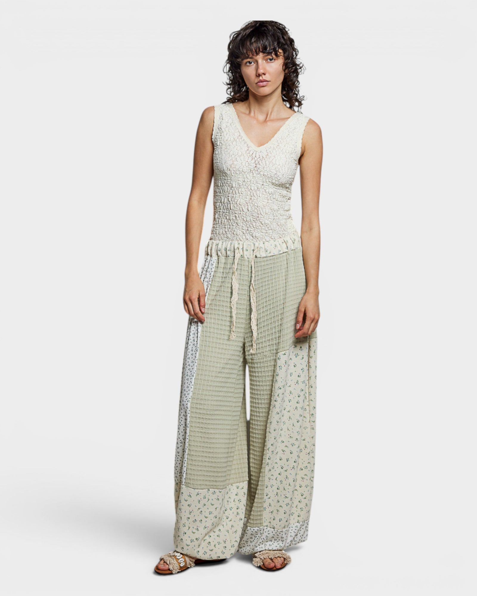 Woman wearing a sleeveless top and wide-leg pants with a white background