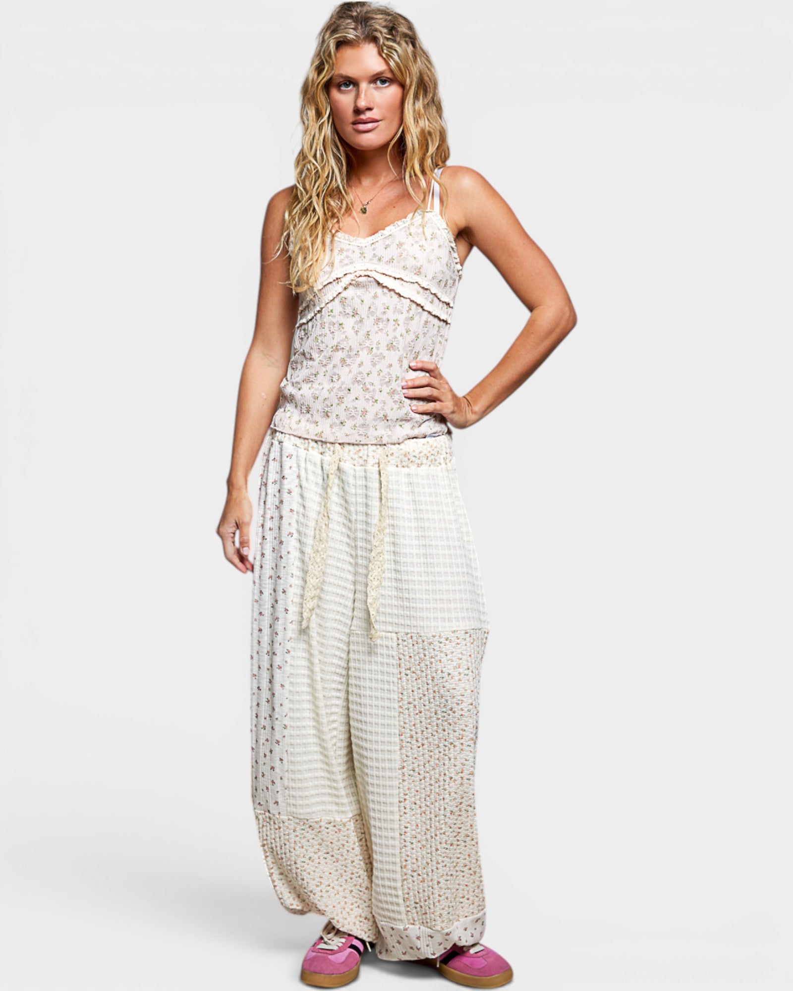 Woman wearing white patterned pants and top on a plain background