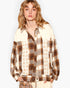 A model wearing a long-sleeve button-up shirt with a mixed pattern design, featuring a brown and beige plaid pattern on one side and a cream base with tan stars on the other.