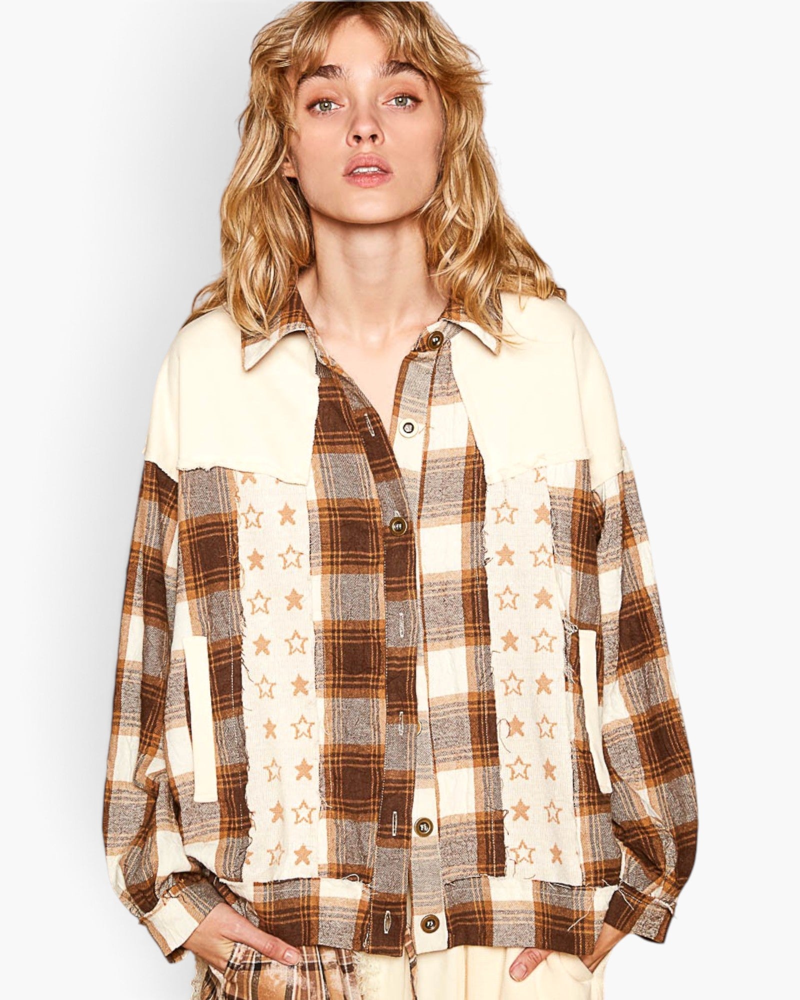 A woman wearing a patchwork button-up shirt with cream, brown, and tan plaid panels, star print, and solid cream shoulder yokes, photographed against a light gray studio background.