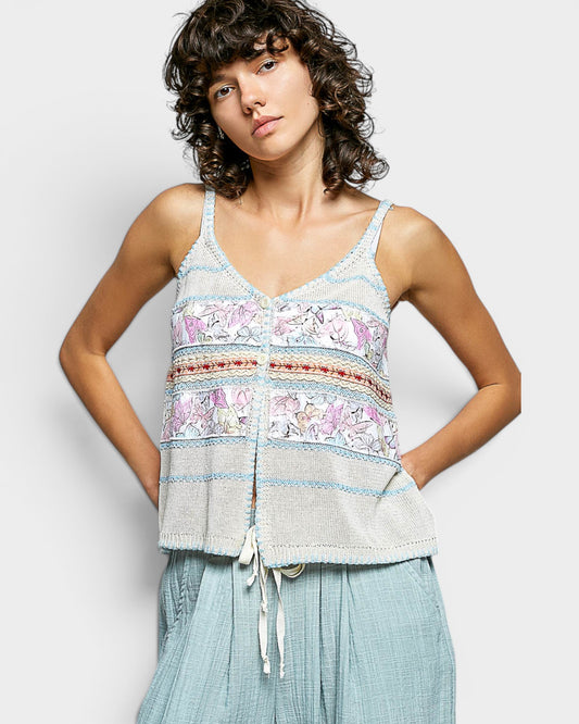 Woman wearing a patterned tank top and light blue pants against a white background