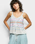Woman wearing a patterned tank top and light blue pants against a white background