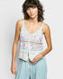 Woman wearing a patterned sleeveless top and light blue pants on a plain background