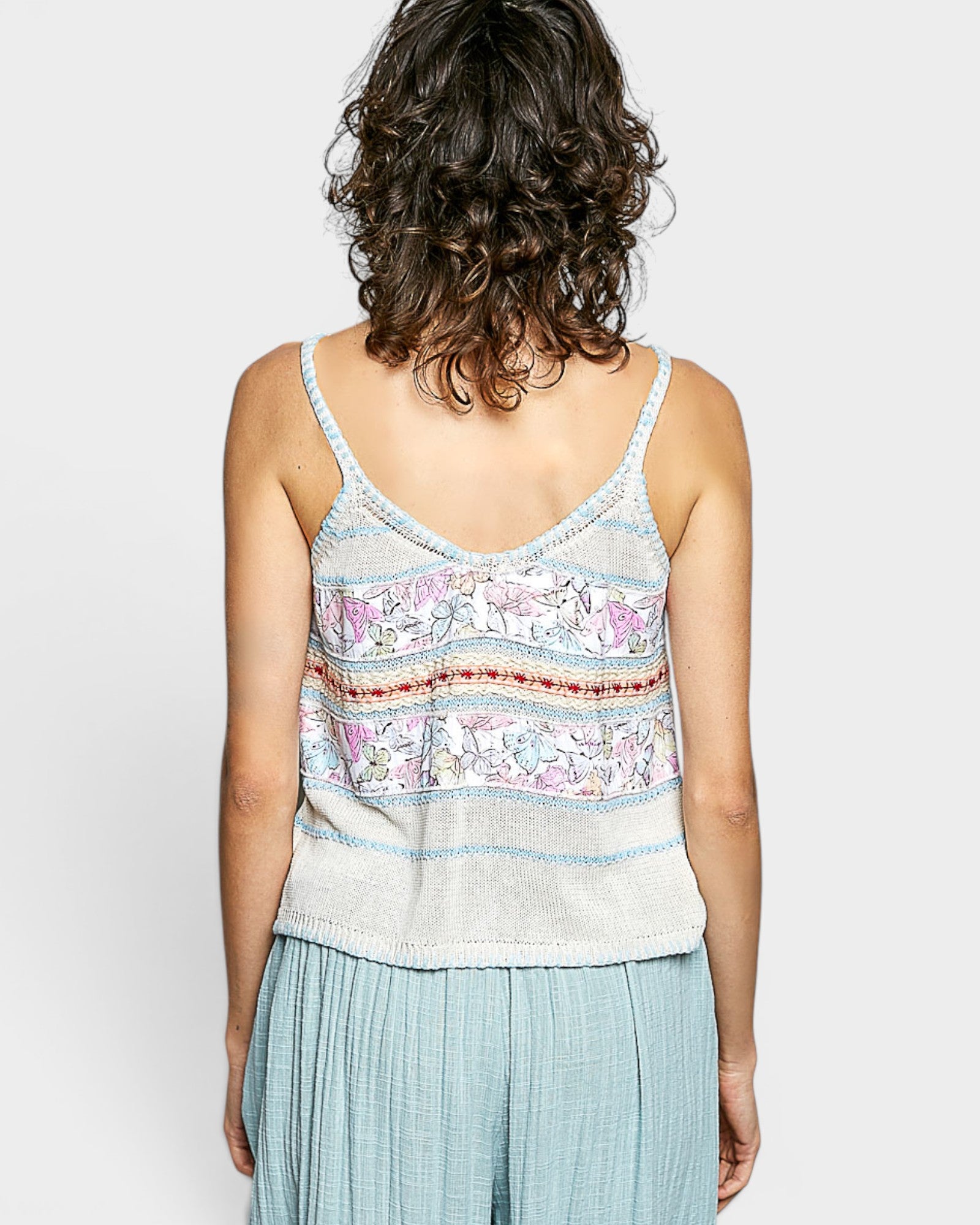 Person wearing a patterned tank top and light blue pants on a plain background