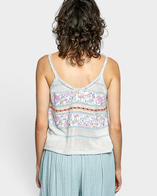 Person wearing a patterned tank top and light blue pants on a plain background