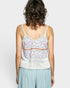 Person wearing a patterned tank top and light blue pants on a plain background