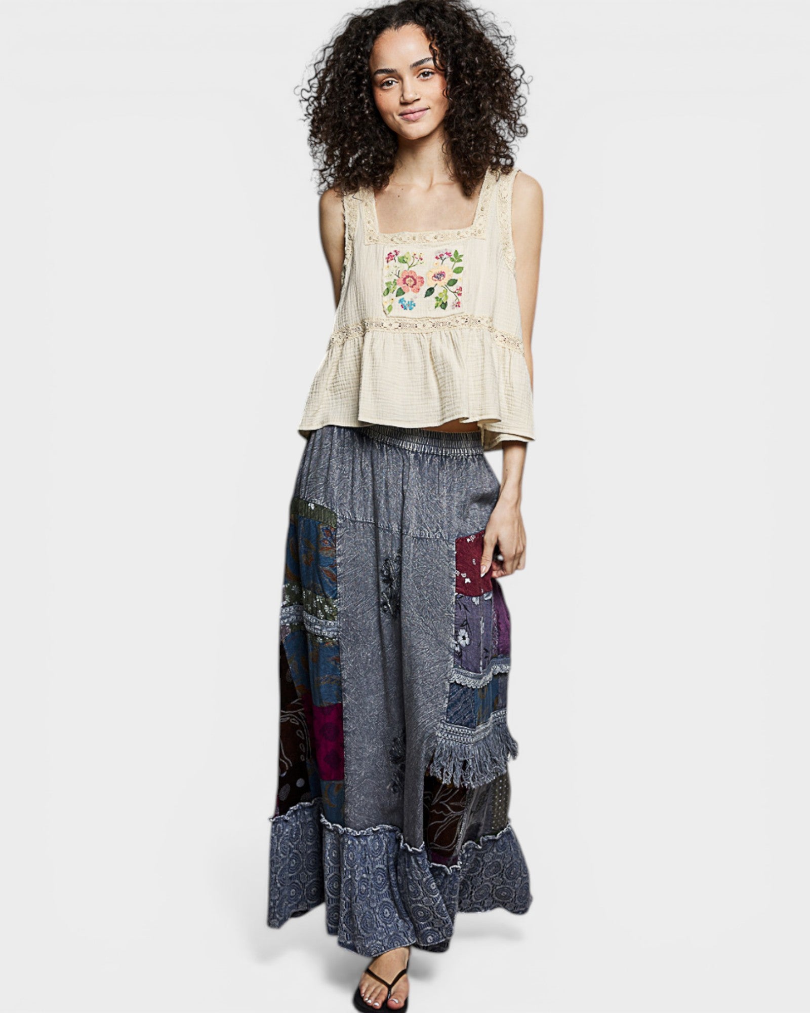 Woman wearing a beige embroidered top and a long, patterned skirt on a white background