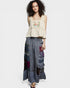 Woman wearing a beige embroidered top and a long, patterned skirt on a white background