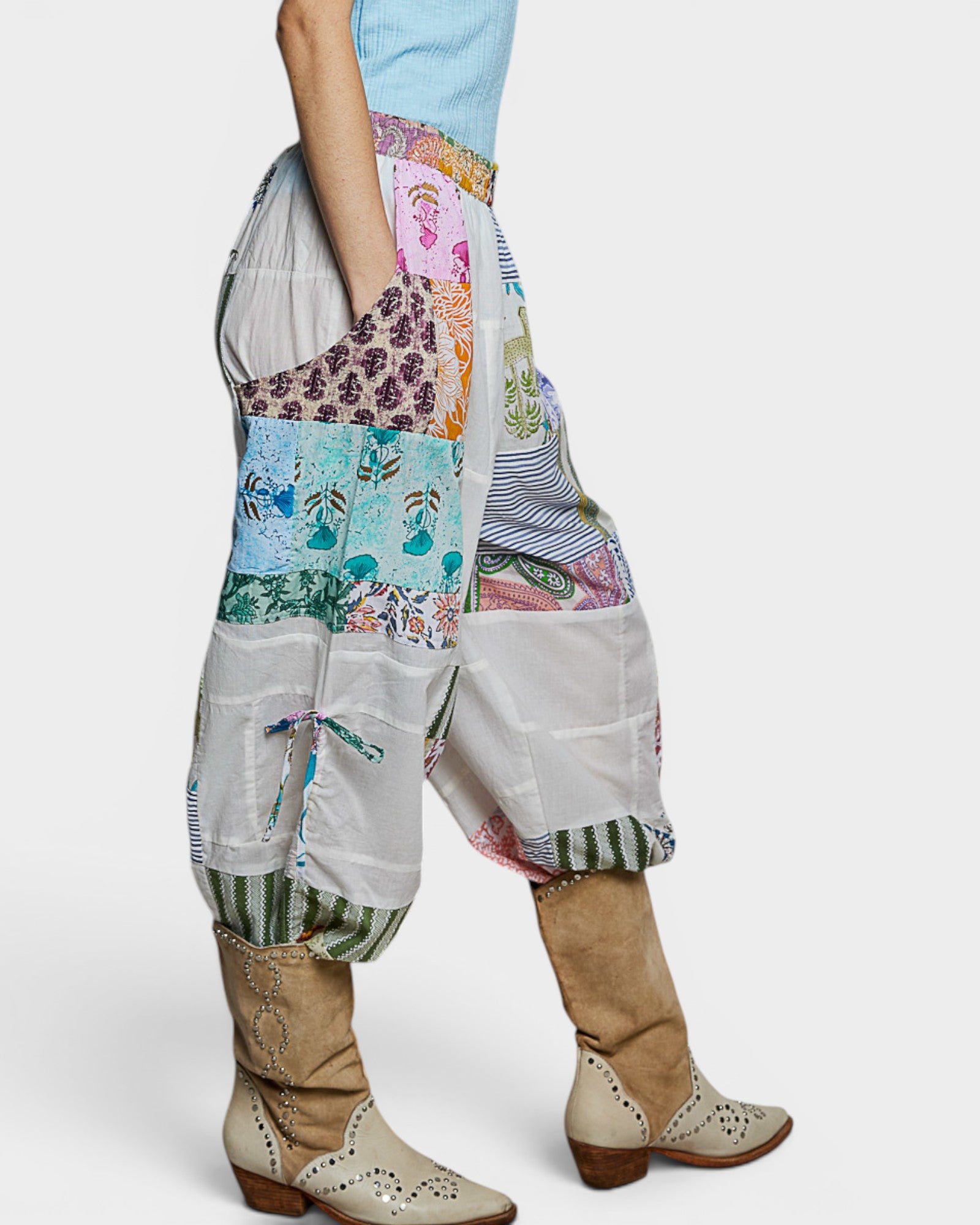 Person wearing a colorful patchwork outfit with high-waisted pants and boots on a white background