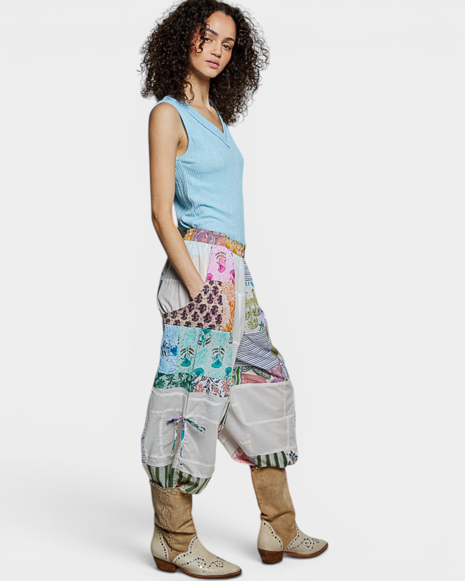 Woman wearing a light blue sleeveless top and colorful patchwork pants on a white background