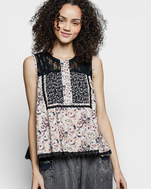 Woman wearing a sleeveless top with floral and lace patterns on a plain background