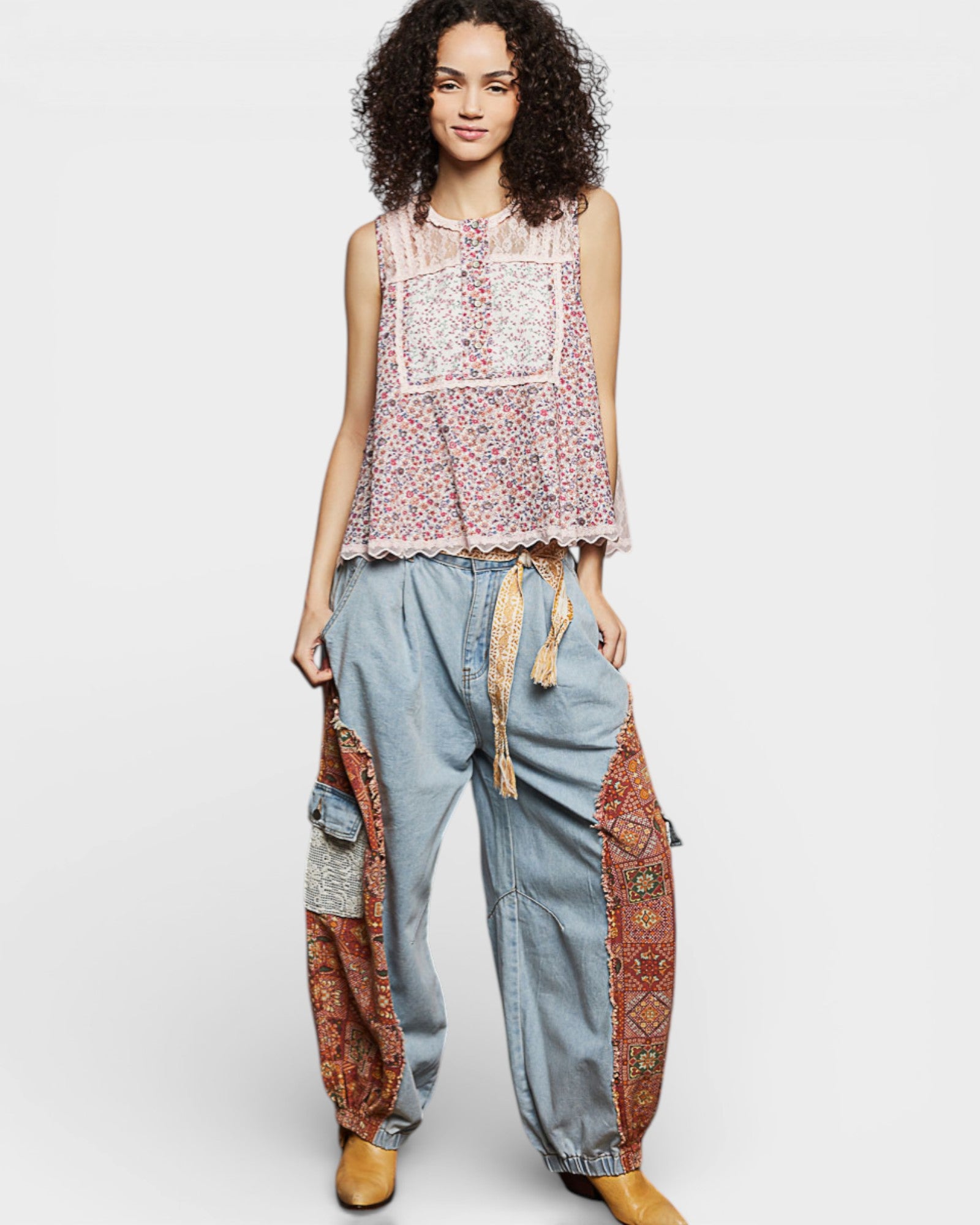 Woman wearing a sleeveless top with floral pattern and high-waisted jeans with patterned patches on a white background