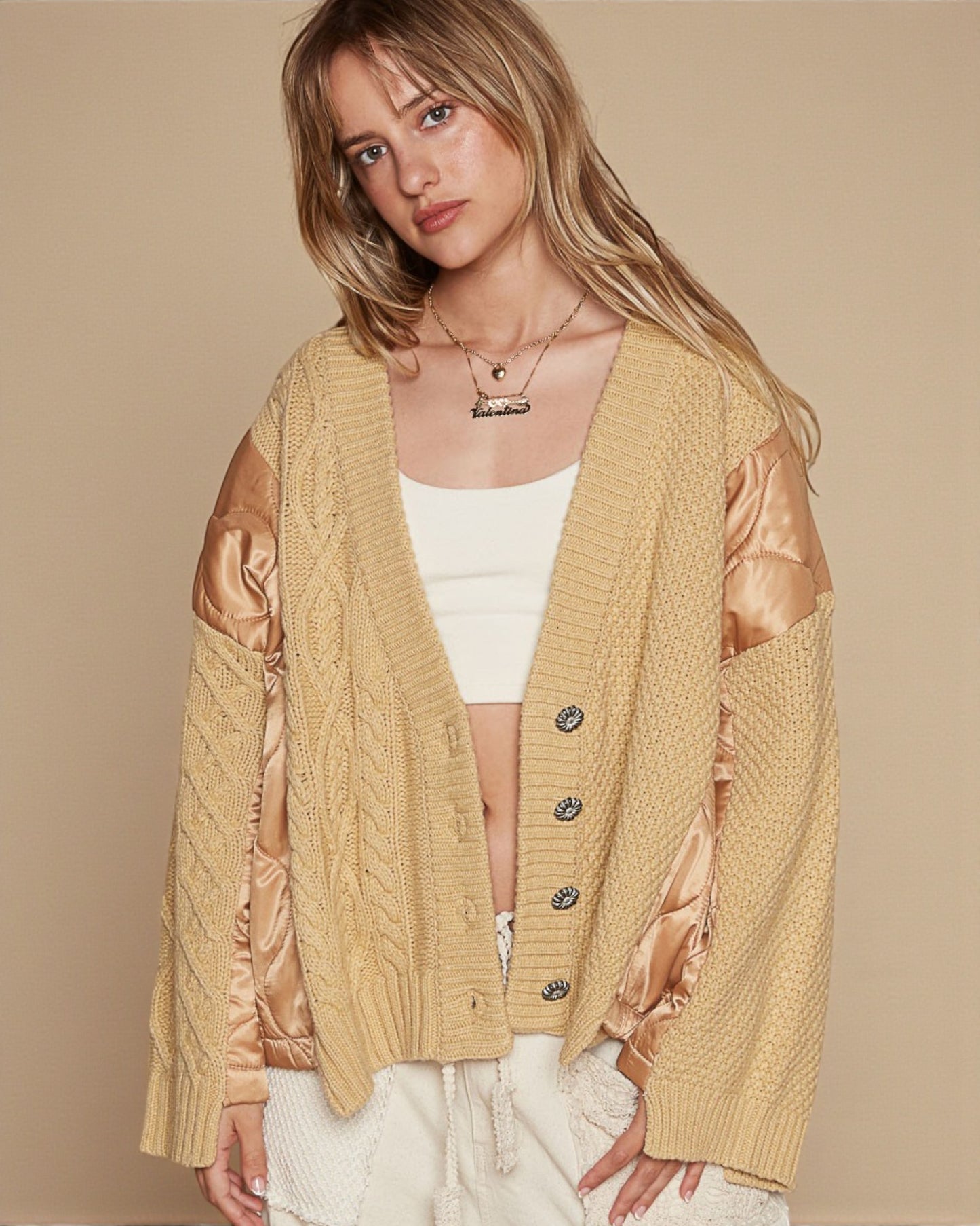 Woman wearing a beige cardigan with satin sleeves on a beige background