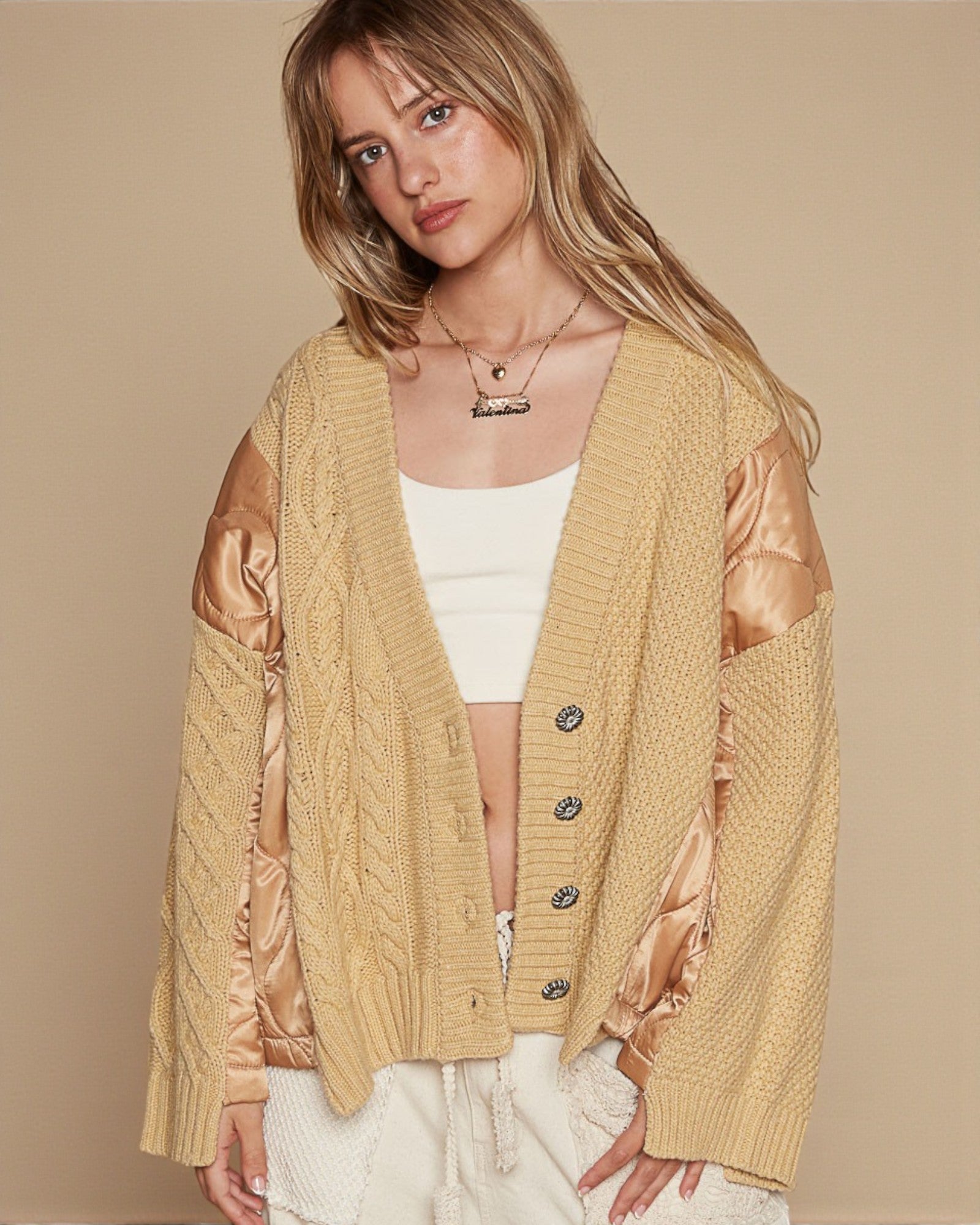 Woman wearing a beige cardigan with satin sleeves on a beige background