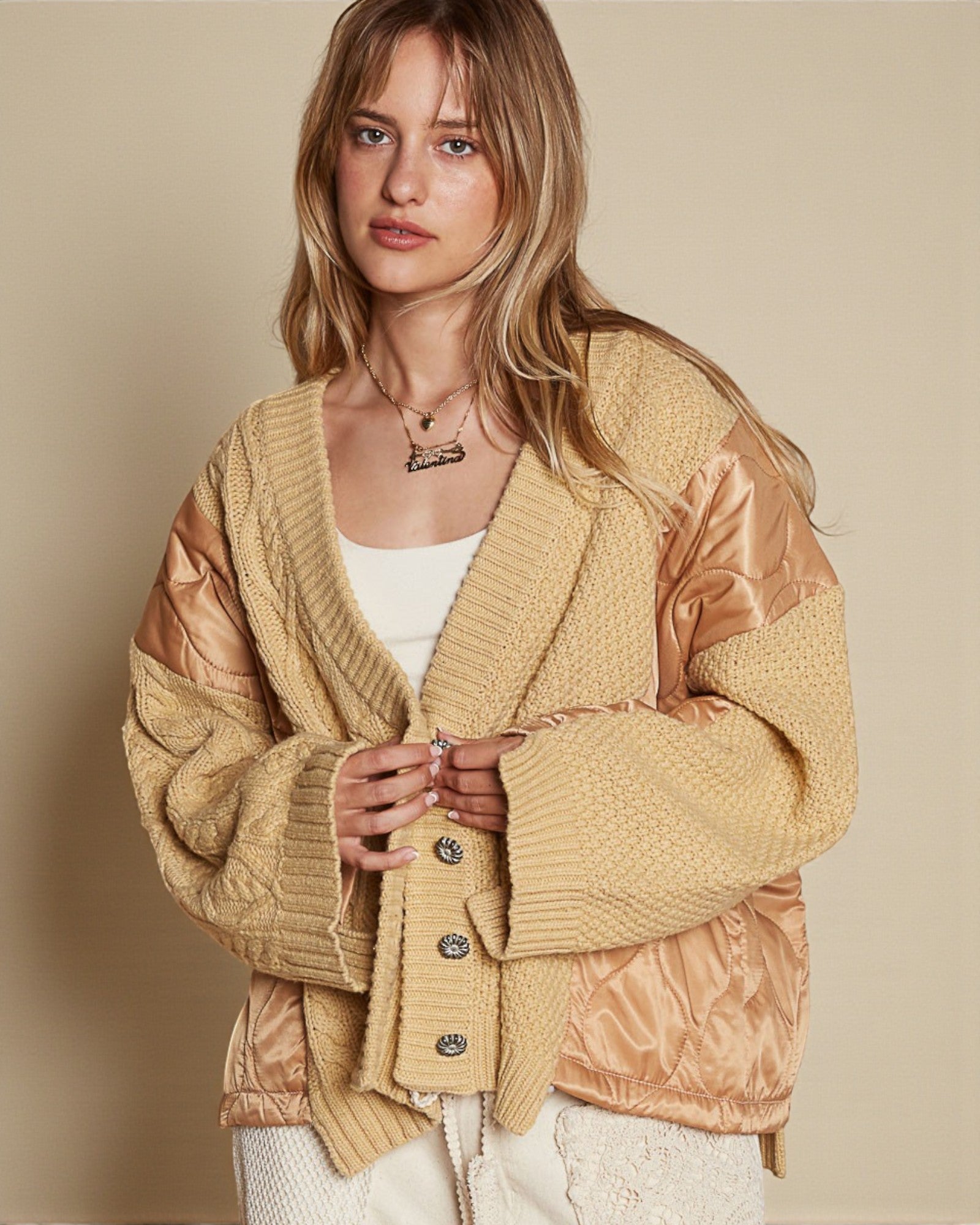 Woman wearing a beige cardigan with brown accents on a beige background