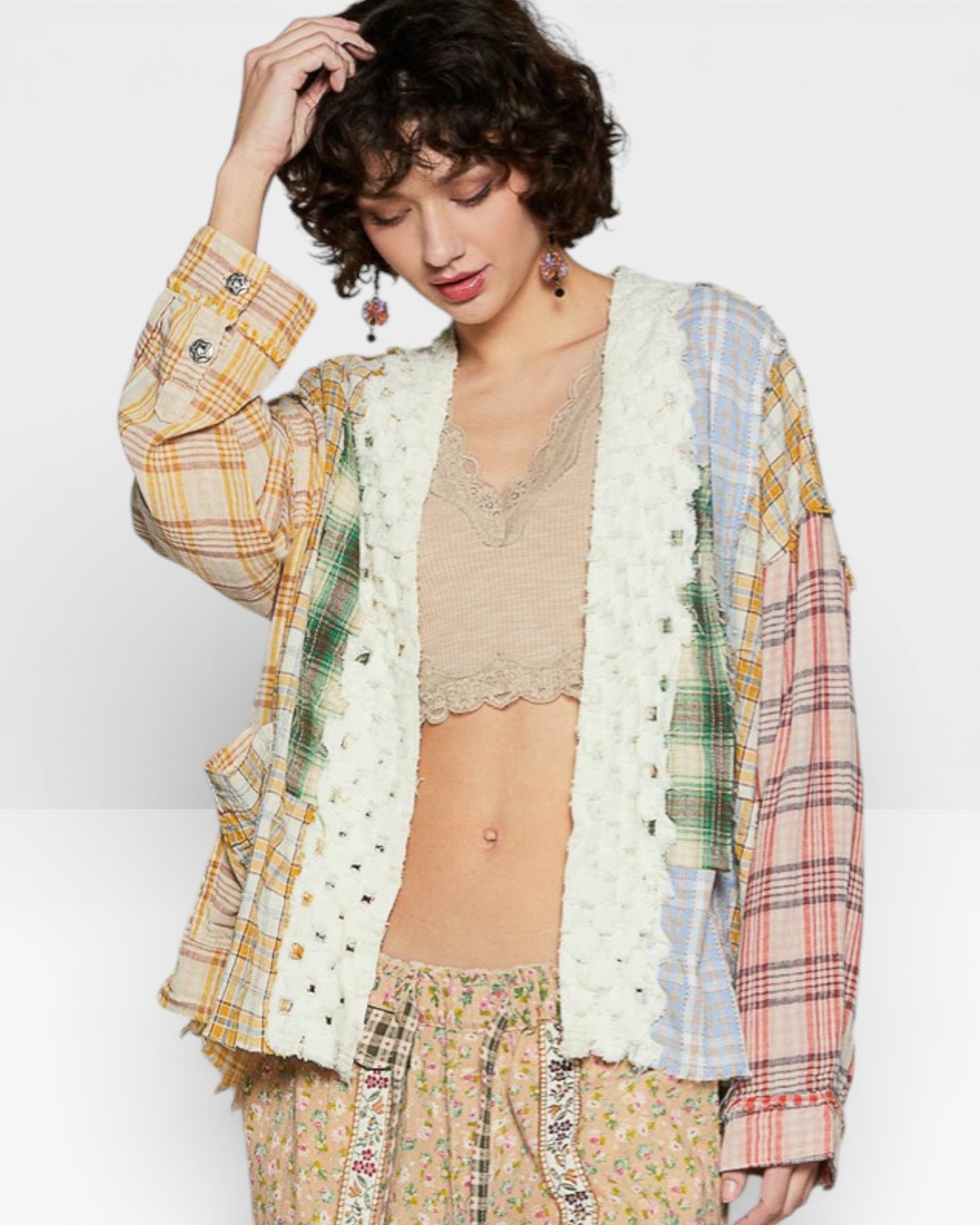 Woman wearing a plaid shirt over a lace top and floral pants on a white background