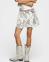 Person wearing a floral skirt and white cowboy boots on a plain background