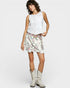 Woman wearing a white sleeveless top and floral skirt with white cowboy boots on a white background