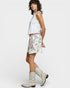 Woman wearing a white sleeveless top and floral skirt with white cowboy boots on a white background