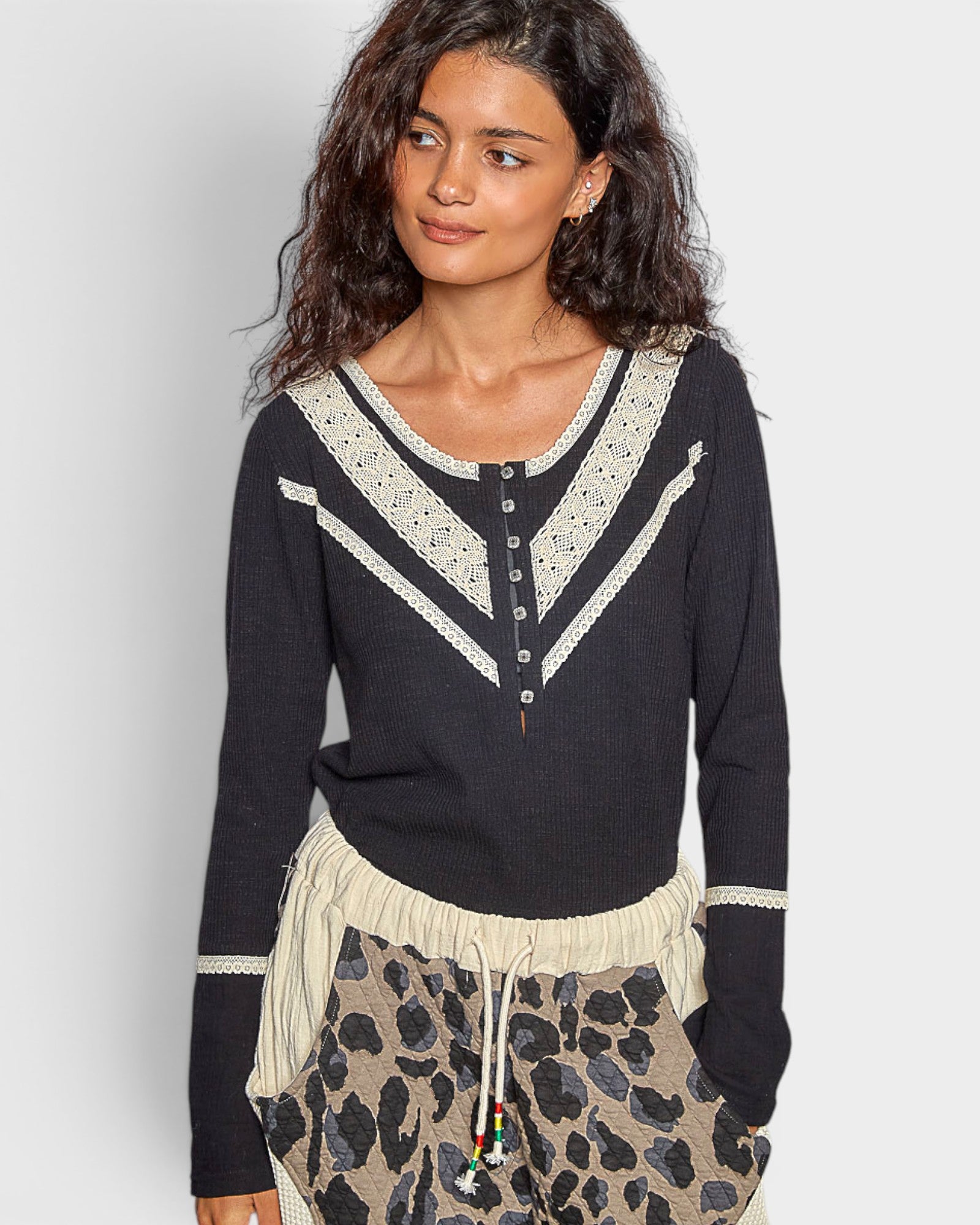 Woman wearing a black sweater with white lace details on a plain background
