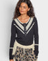 Woman wearing a black sweater with white lace details on a plain background