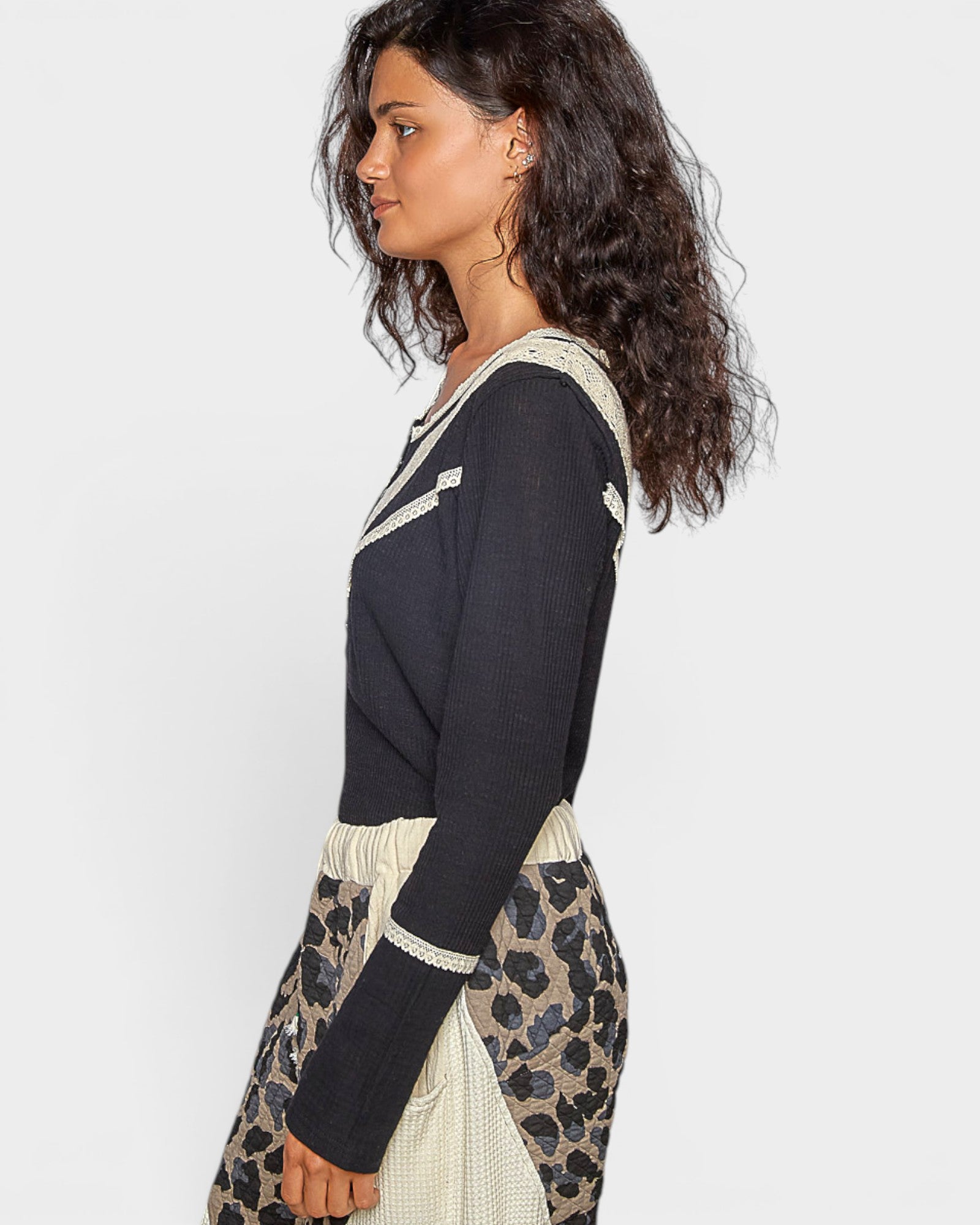 Woman wearing a black long-sleeve top with white trim and leopard print pants on a light gray background