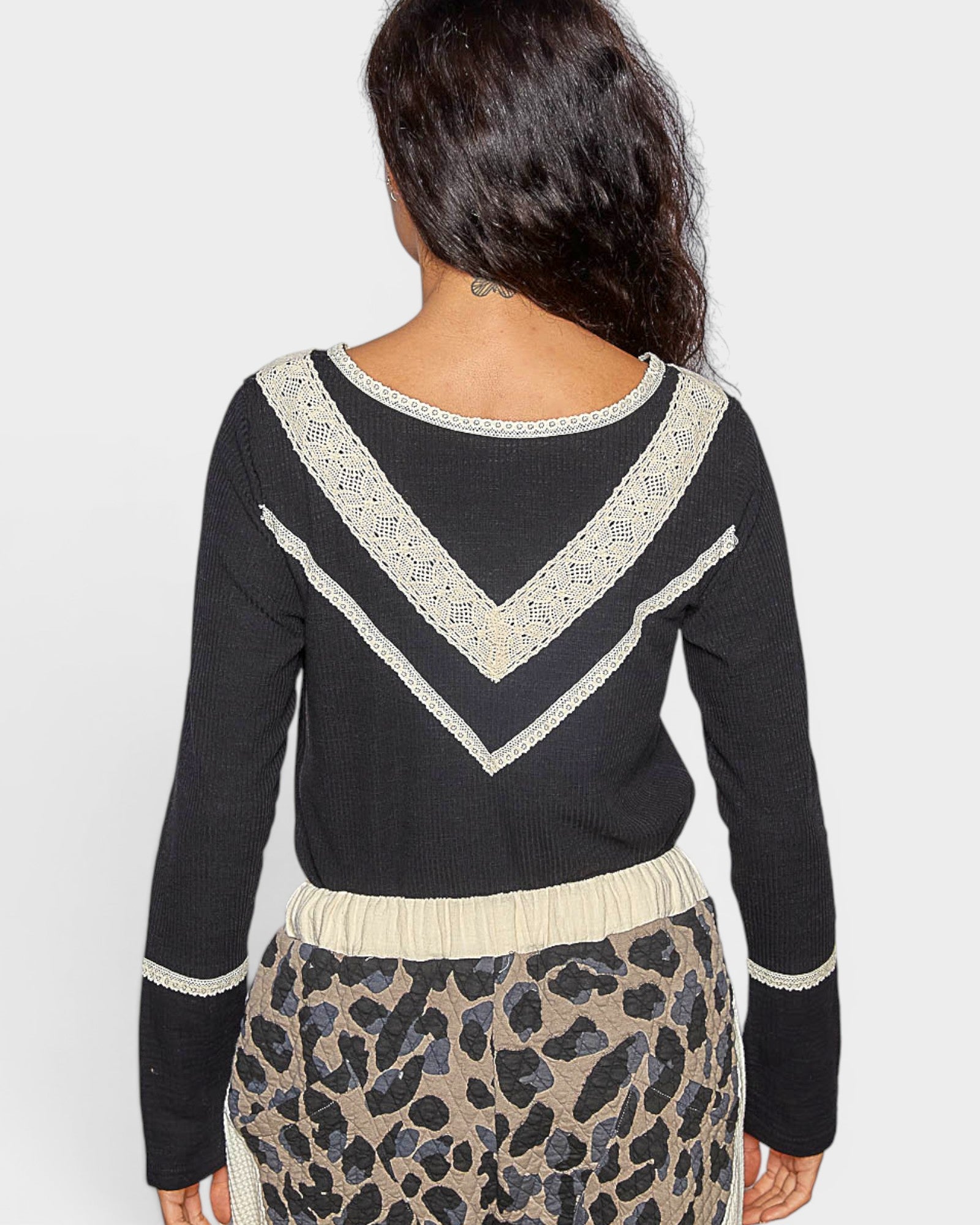 Person wearing a black sweater with white lace details and a leopard print skirt on a light gray background