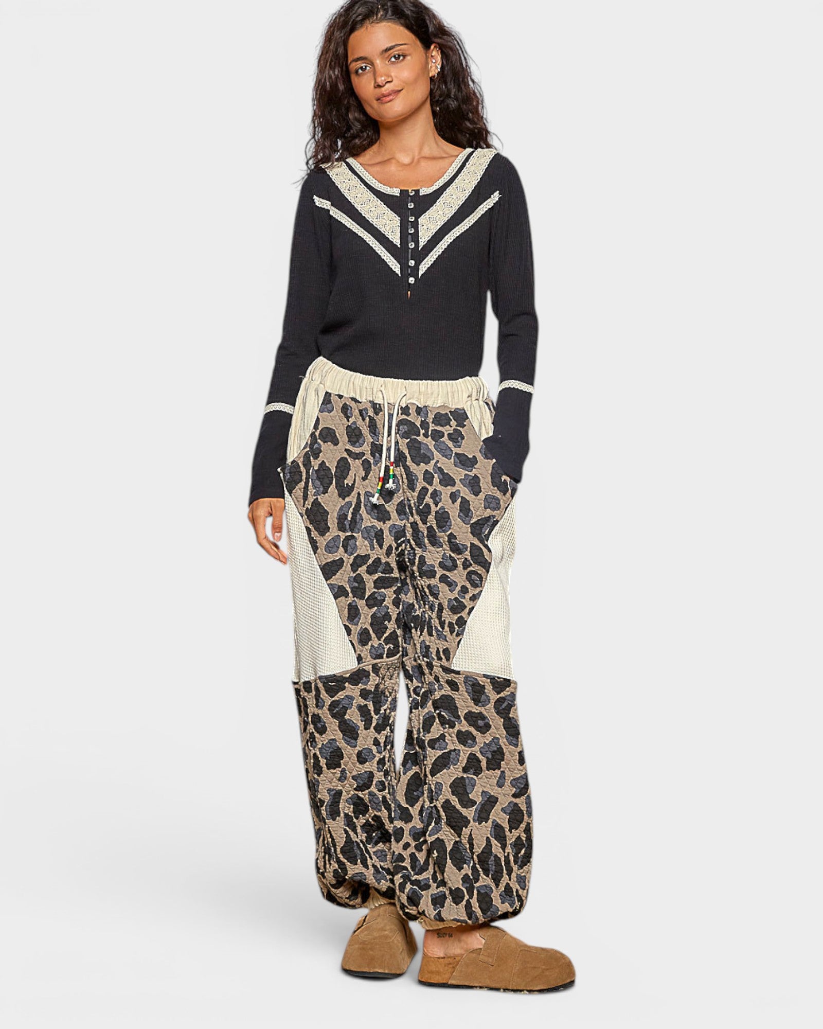 Woman wearing a black top with white trim and leopard print pants on a white background