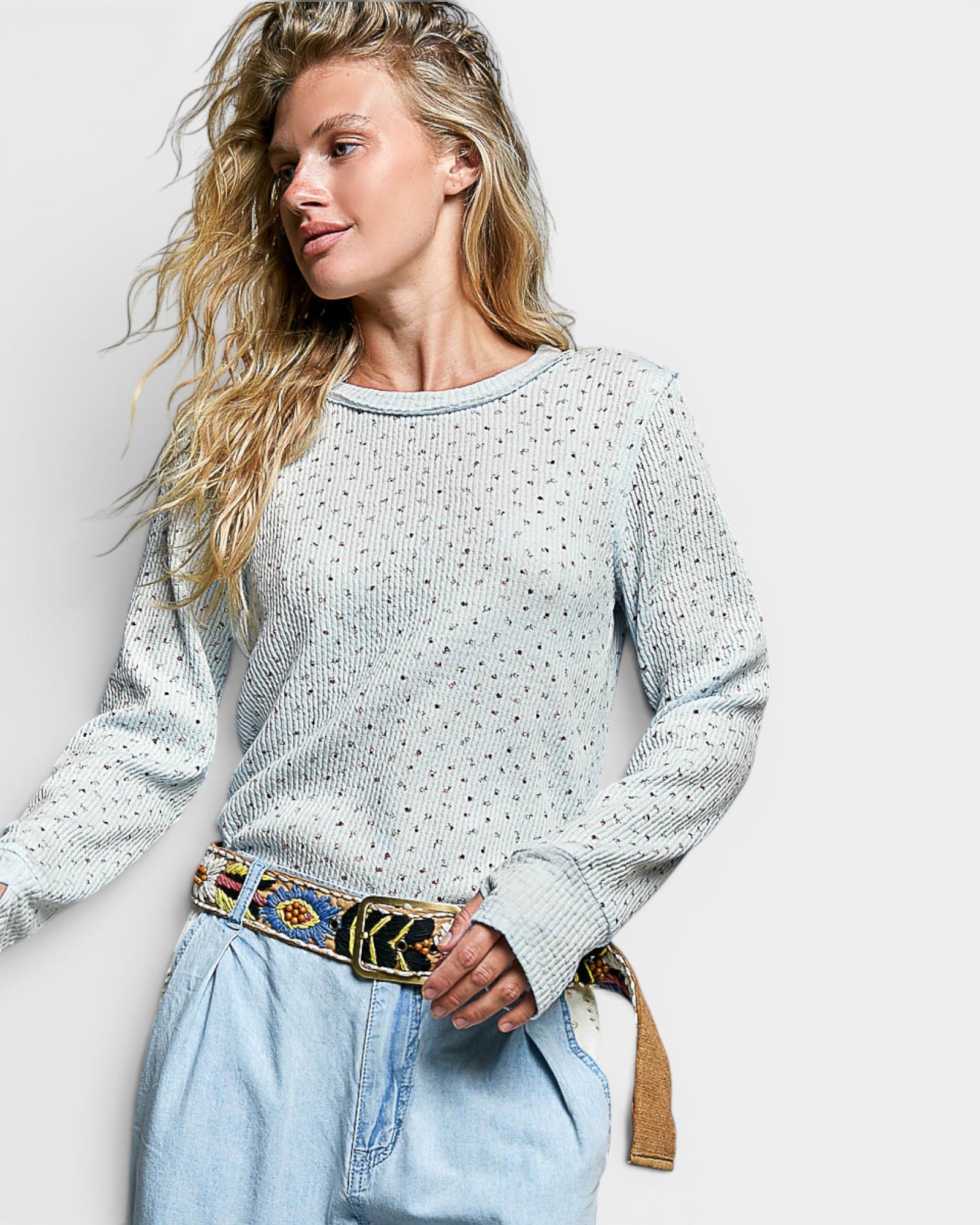 Woman wearing a patterned sweater and light blue jeans with a decorative belt against a plain background