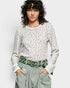 Person wearing a patterned sweater and green pants with a floral belt on a white background