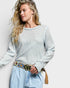 Woman wearing a patterned sweater and light blue jeans with a decorative belt against a plain background