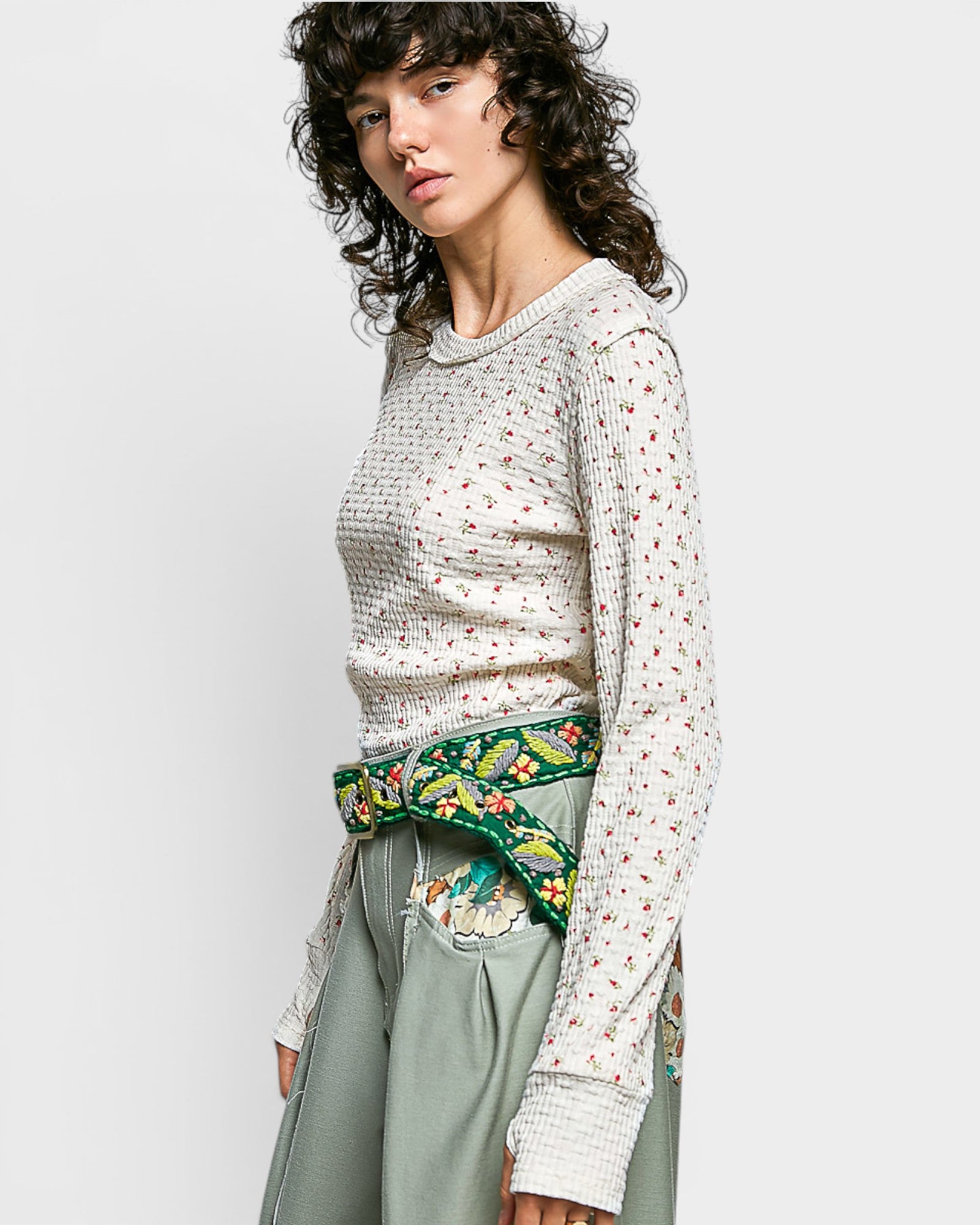 Woman wearing a patterned top and green embroidered belt against a plain background
