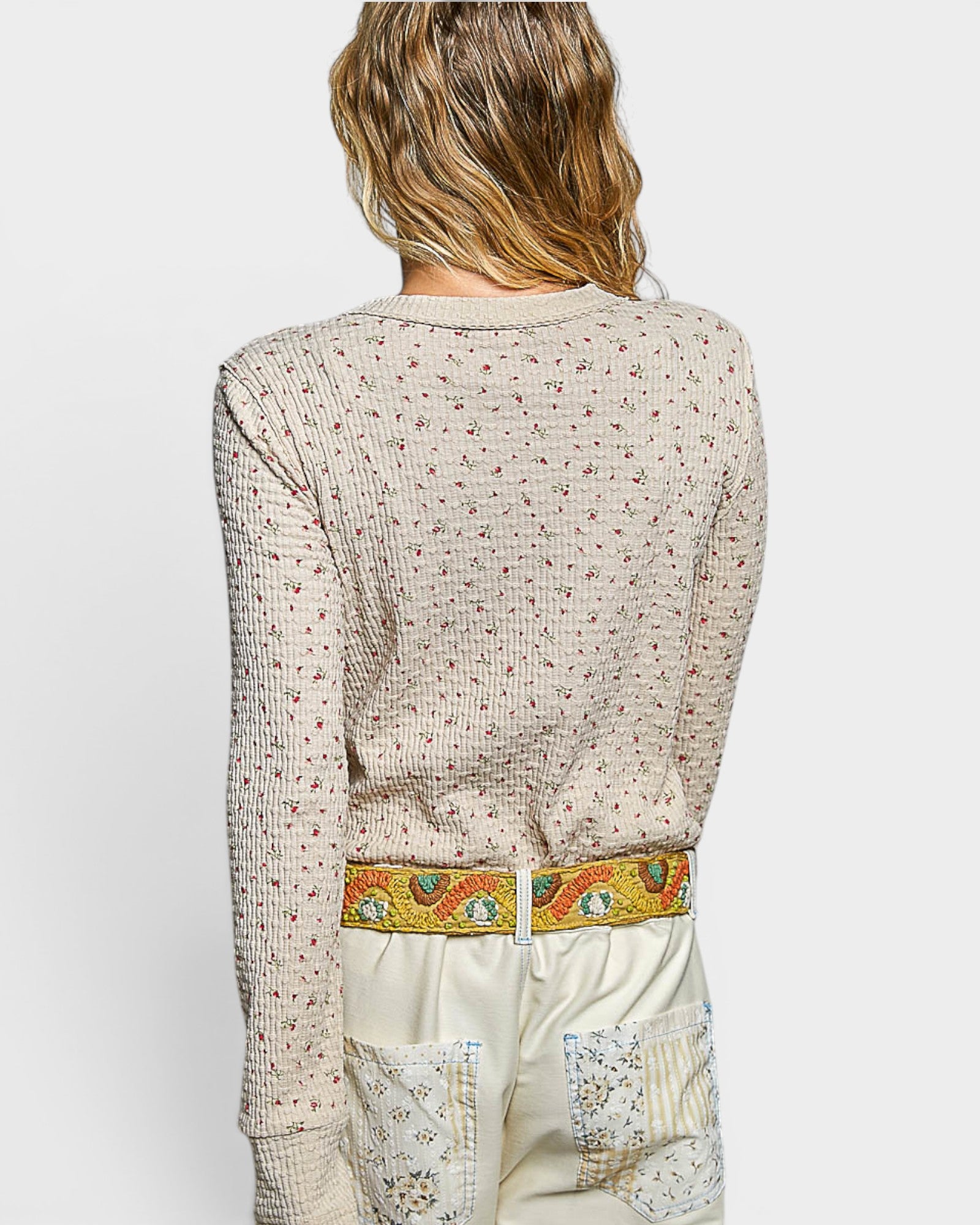Person wearing a patterned top with a colorful belt and white pants on a light background