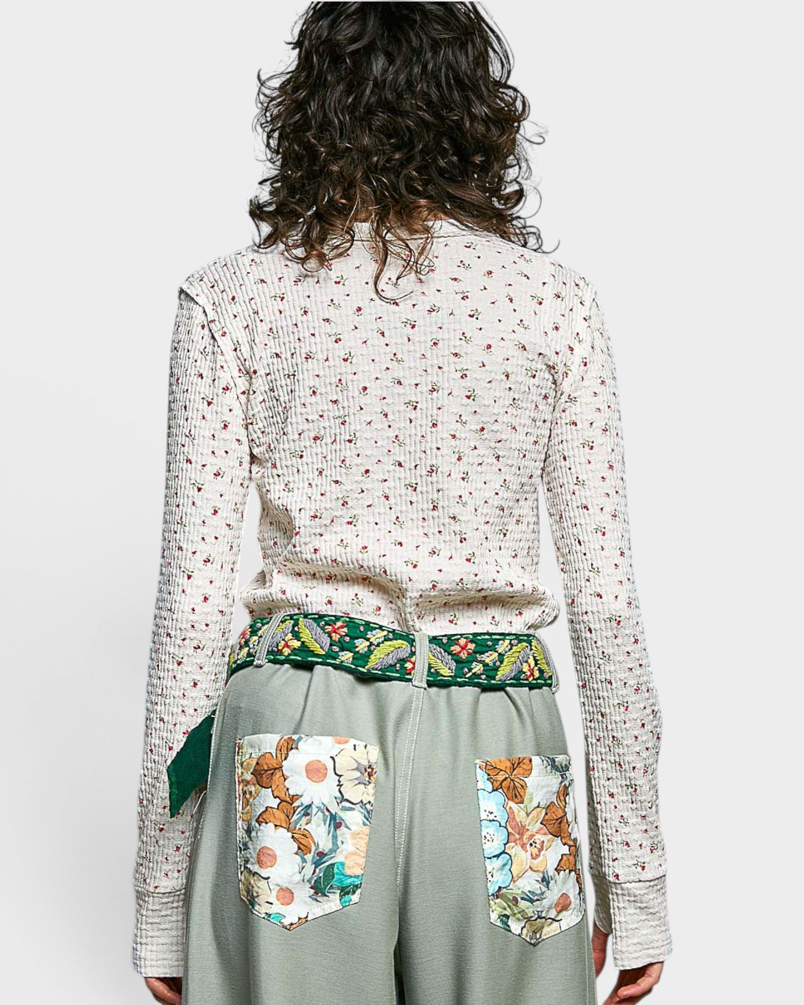 Person wearing a floral-patterned top and green skirt with floral pockets on a white background