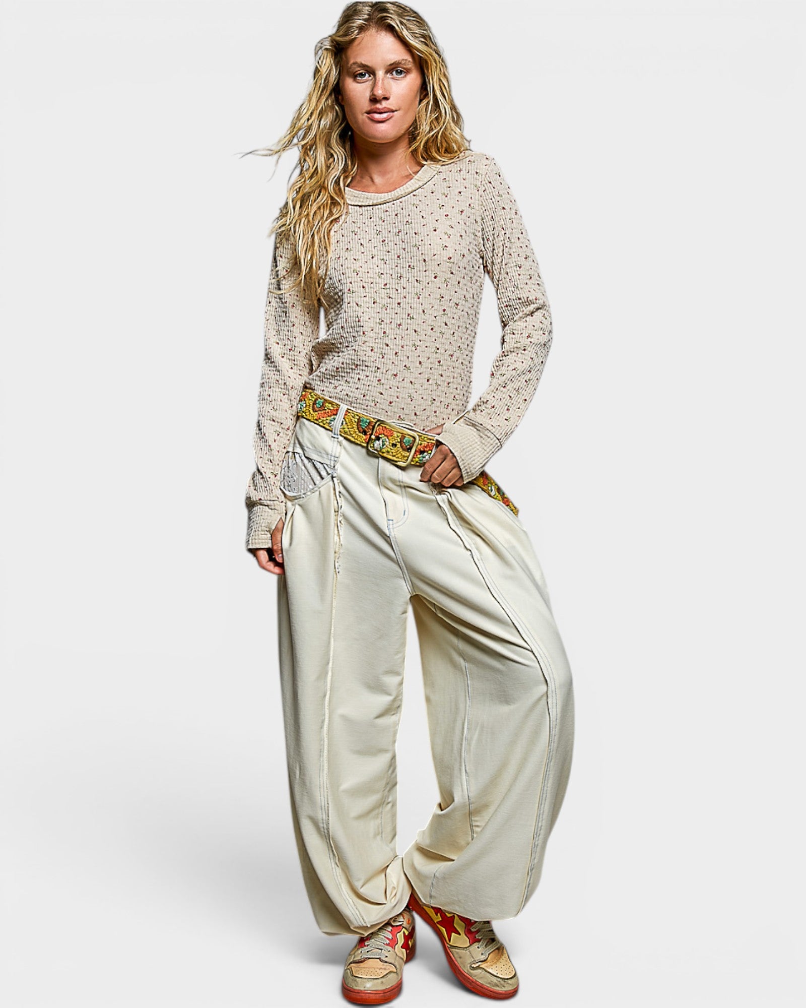 Woman wearing a patterned sweater and wide-leg pants with a colorful belt on a white background