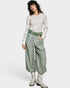 Woman wearing a patterned top and green pants with embroidery, standing against a white background