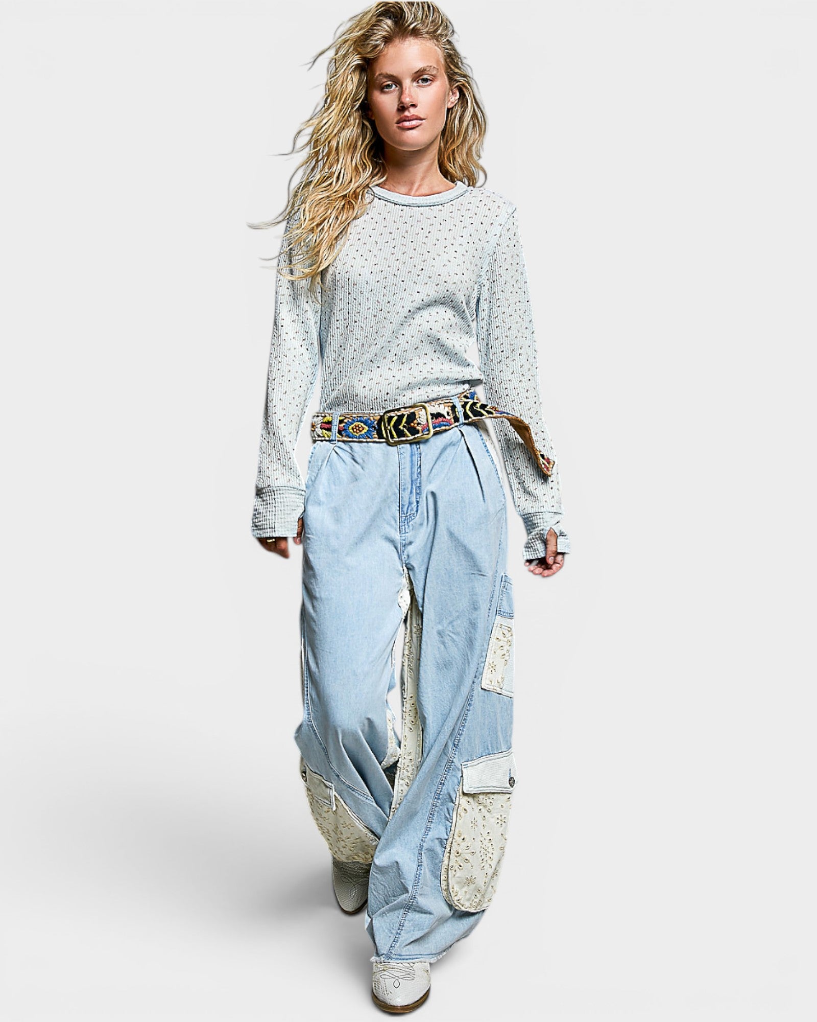 Woman wearing a light blue patterned top and light blue patchwork pants on a white background