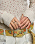 Close-up of hands adjusting a floral-patterned belt with an owl design.