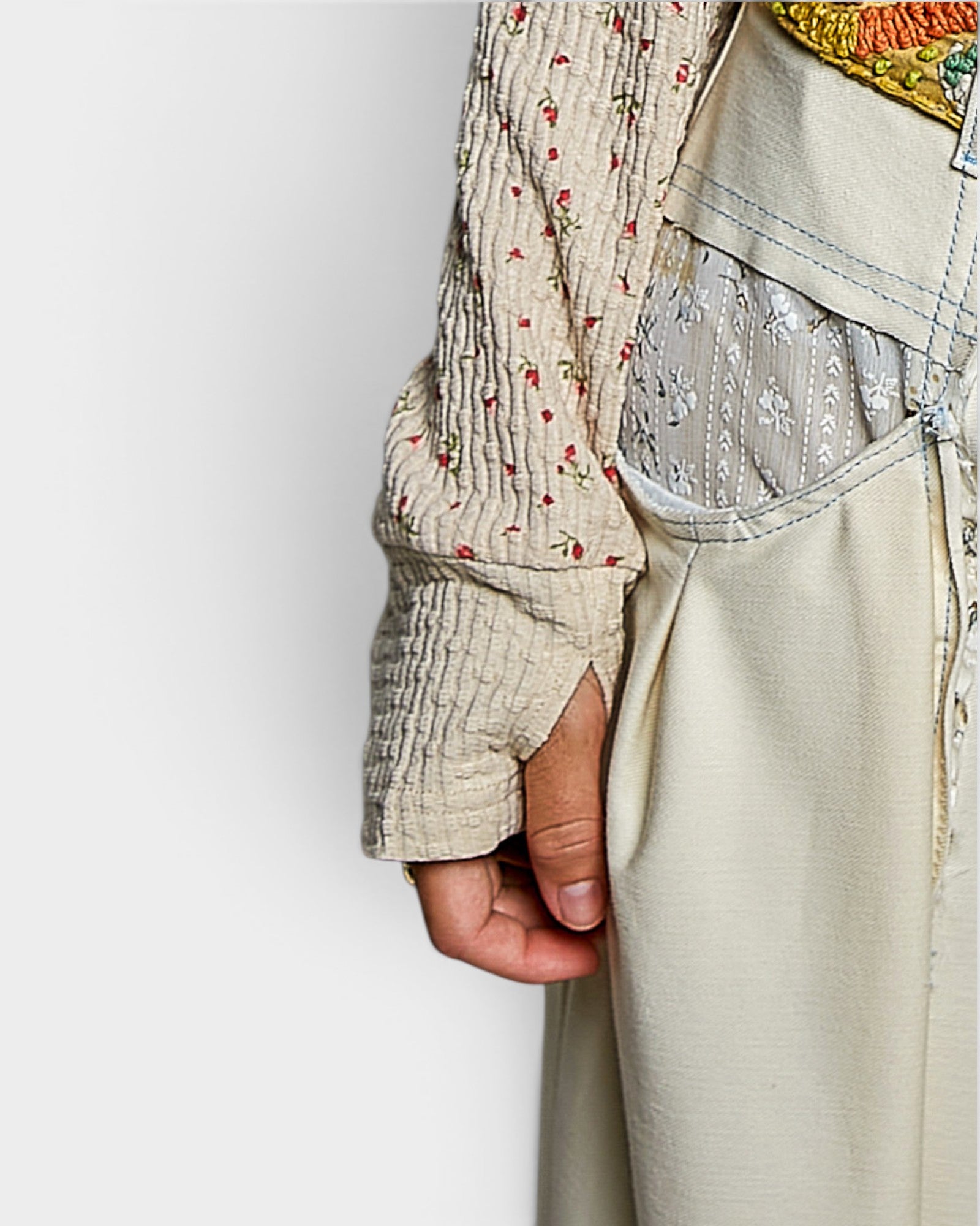 Close-up of a person wearing a patterned shirt and light-colored pants against a plain background