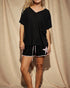 Person wearing a black ribbed top and black shorts with white trim against a beige curtain background